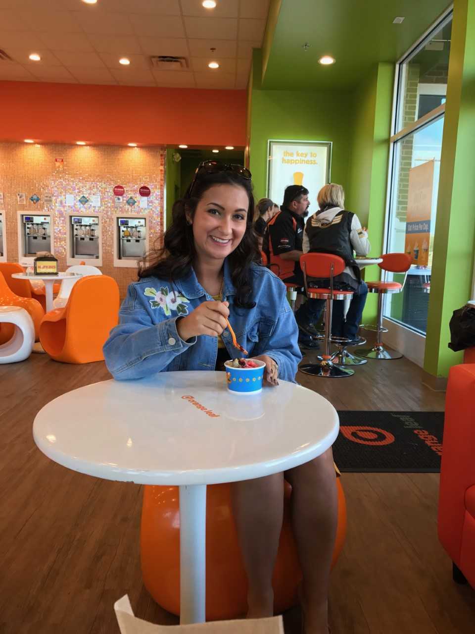 A smiling female posing with frozen yogurt while sitting in a colorful frozen yogurt shop